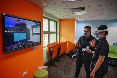 MANFAATKAN TEKNOLOGI REALITI MAYA: Jurulatih Besar, Komand Latihan Penguasa Imigresen dan Pusat Pemeriksaan (ICA), ASP Sophia Ng kelihatan sedang menjalani simulasi mengendali sebuah kelas Realiti Maya (VR) sambil menerima bimbingan oleh Eksekutif Kanan (Perancangan Kurikulum), Pusat bagi Sistem Pembelajaran Akademi Home Team, Encik Ian Koh. - Foto-foto BH oleh JASON QUAH