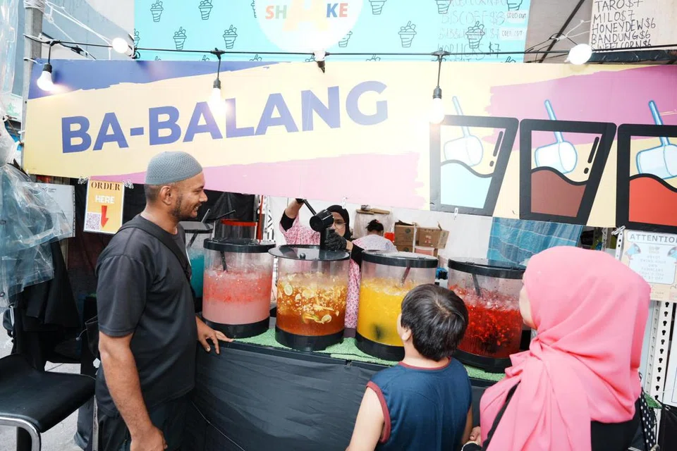 Pemilik reruai minuman Ba-Balang, Encik Muhammad Ali Ibrahim (kiri), memerhatikan minuman air dituangkan  isterinya, Cik Nurenawaty Bahari, ke dalam bekas air keluli tahan karat ‘Save The Earth – Dirgahayu Duniaku’ milik seorang pelanggan.