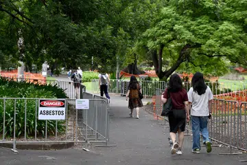 Pengunjung taman melintas lalu papan tanda asbestos yang dipasang di Victoria Park, Sydney, selepas bahan toksik itu ditemui pada 14 Februari.