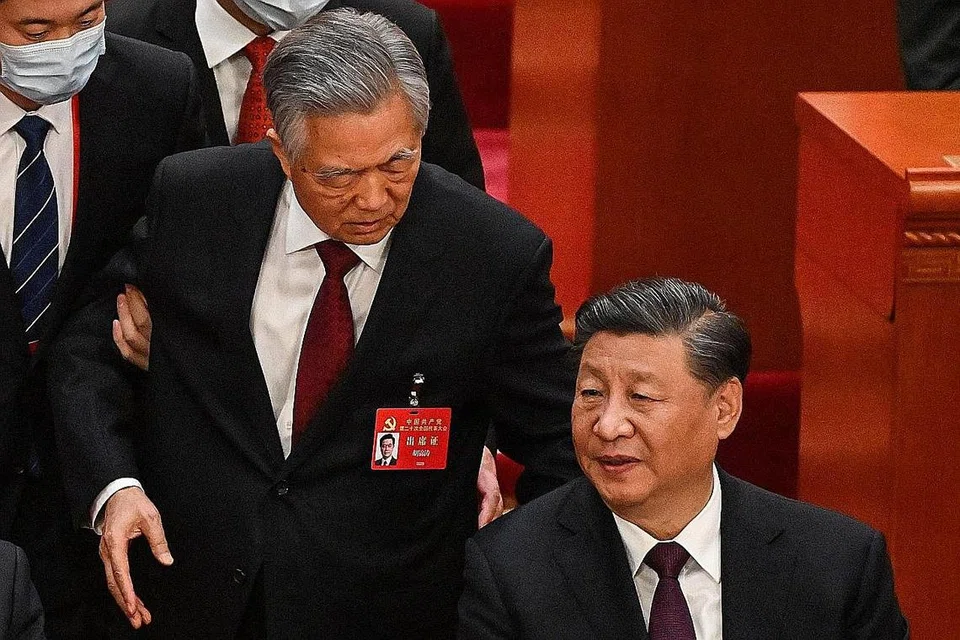 DIIRING KELUAR: Encik Hu Jintao (tengah) berbalas kata dengan Encik Xi Jinping (kanan) sebelum beliau dibawa keluar oleh dua lelaki. - Foto AFP