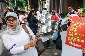A woman bangs kitchen utensils during a protest demanding the government review the free meal program, lower fuel prices, and open more job opportunities for women, in Jakarta on June 18, 2026. (Photo by BAY ISMOYO / AFP)