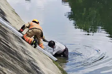 SELAMAT: Seorang lelaki kelihatan ditarik keluar dari terusan oleh seorang pegawai SCDF.
