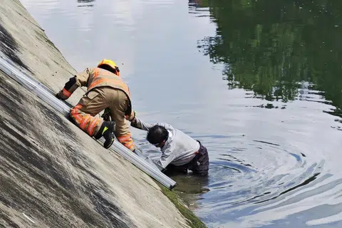 SELAMAT: Seorang lelaki kelihatan ditarik keluar dari terusan oleh seorang pegawai SCDF.