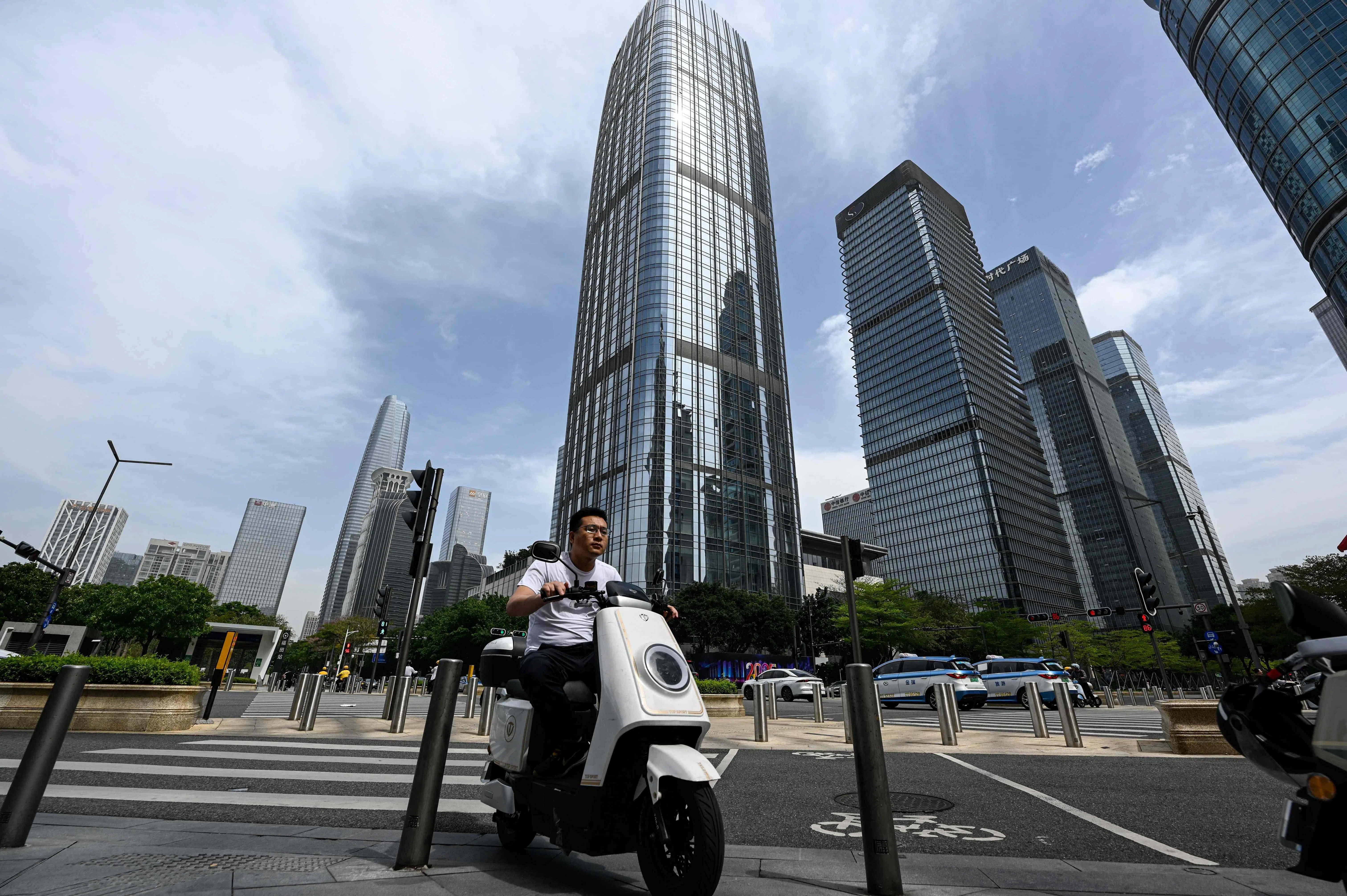 A man rides a scooter at the financial district in Shenzhen, in southern China’s Guangdong Province on April 14, 2025. (Photo by JADE GAO / AFP)