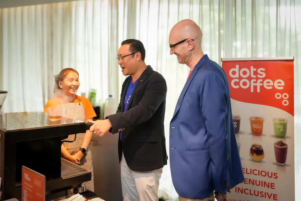 Guillaume Rachou (right), executive director of Save the Children Thailand, and Kanit Sangmookda (centre), country general manager of Thailand and Laos at Ascott, interacting with a visually impaired employee of Dots Coffee.