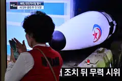 A woman walks past a television screen showing file footage of a North Korean missile test. North Korea test launched two ballistic missiles towards the sea off its east coast on Wednesday.