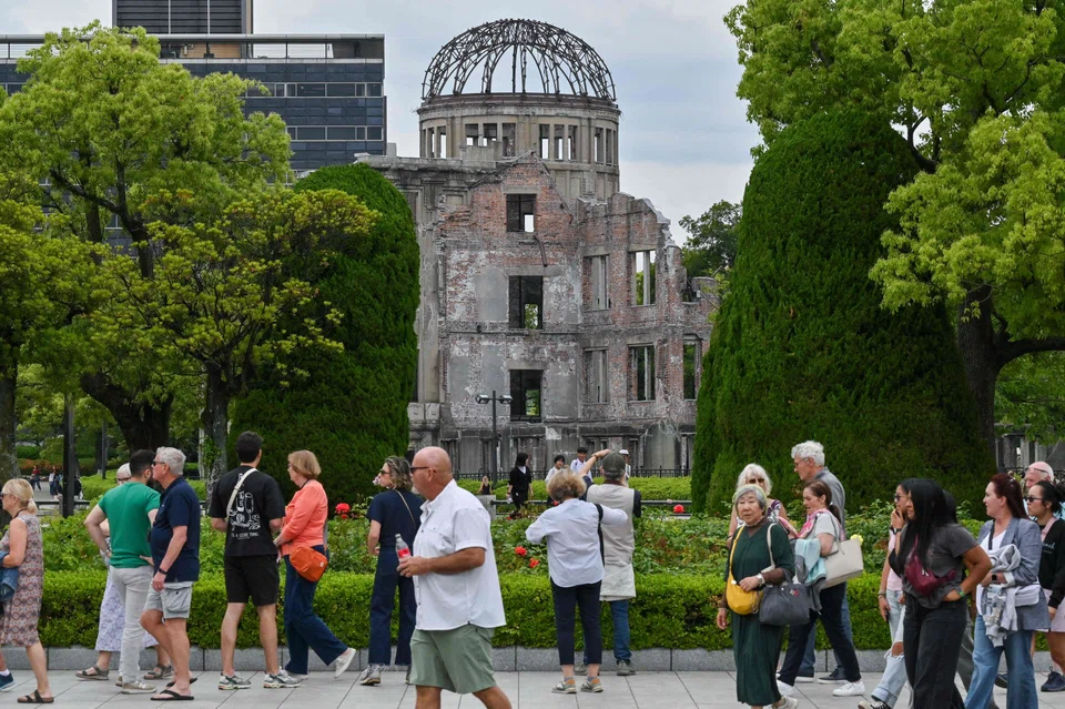 Tourists in the Peace Memorial Park in Hiroshima, with the Atomic Bomb Dome – the only structure that remained standing in the area around the US' atomic bombing of the city on Aug 6, 1945 – in the background. 