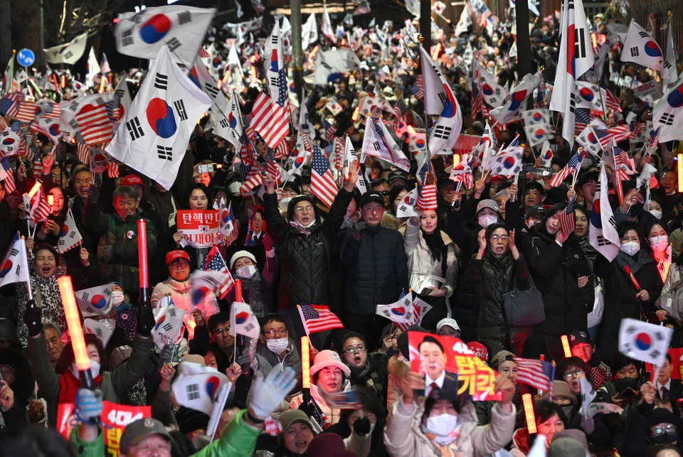 Supporters of impeached South Korean President Yoon Suk Yeol wave South Korean and US flags during a rally near the presidential residence in Seoul on March 8, 2025 after a motorcade carrying Yoon arrived at the residence. 