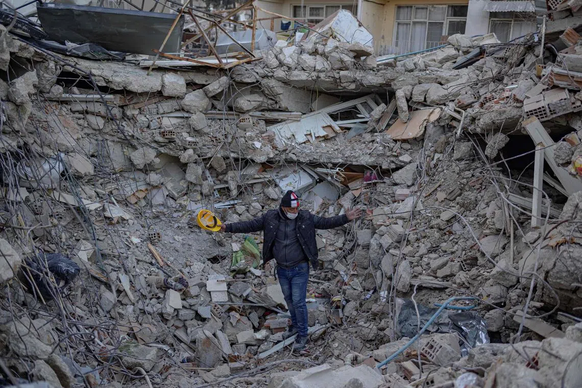 A man stands amid rubble of a collapsed buidling while Greek and Turkish rescuers try to exhume the bodies of six of his relatives, including four children, in Antakya, south of Hatay, on Feb 15, 2023.