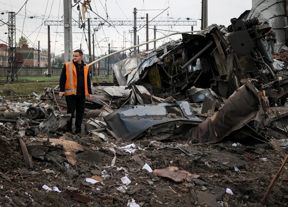A worker stands near train cars at a freight railway station destroyed by Russian military strikes; Kharkiv, Ukraine, Sep 2022.  