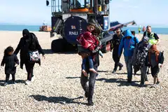 A man carrying a child in his arms is followed by a migrant pregnant woman (second right), as they walk on the beach at Dungeness on the south-east coast of England, on August 16, 2023.