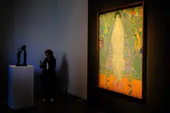The piece depicts the daughter of Klimt’s main patron dressed in a white imperial Chinese dress, standing before a blue tapestry with Asian-inspired motifs.
