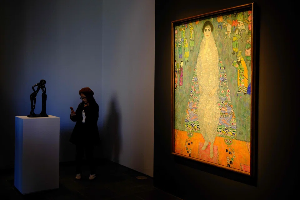 The piece depicts the daughter of Klimt’s main patron dressed in a white imperial Chinese dress, standing before a blue tapestry with Asian-inspired motifs.