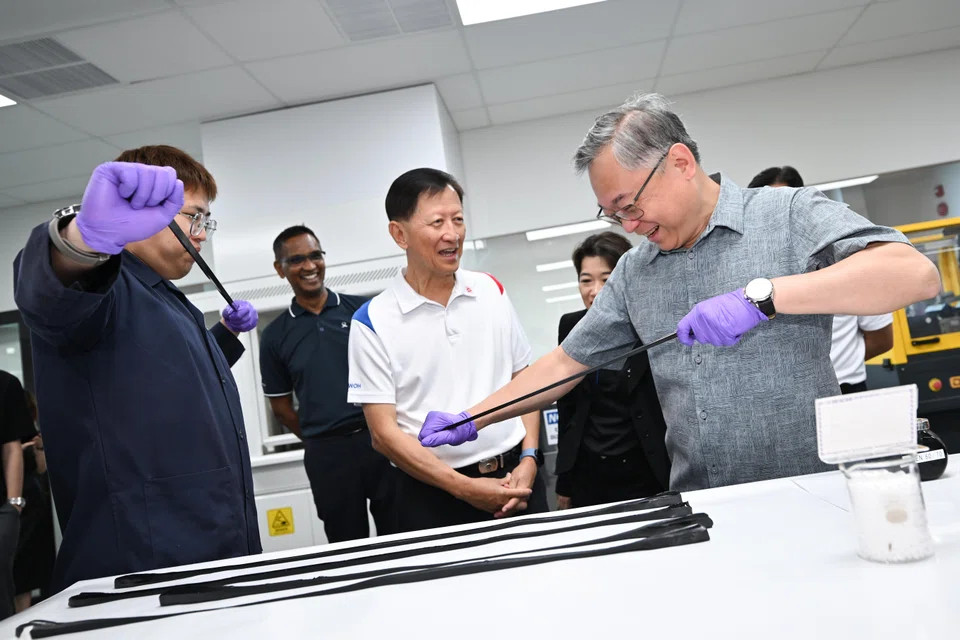 Samwoh executive engineer Chow Wee Kang (left) and Minister for Trade and Industry Gan Kim Yong stretching samples of Samwoh's polymer-modified bitumen, which has improved flexibility. Between them stands Samwoh chief operating officer Ho Nyok Yong.