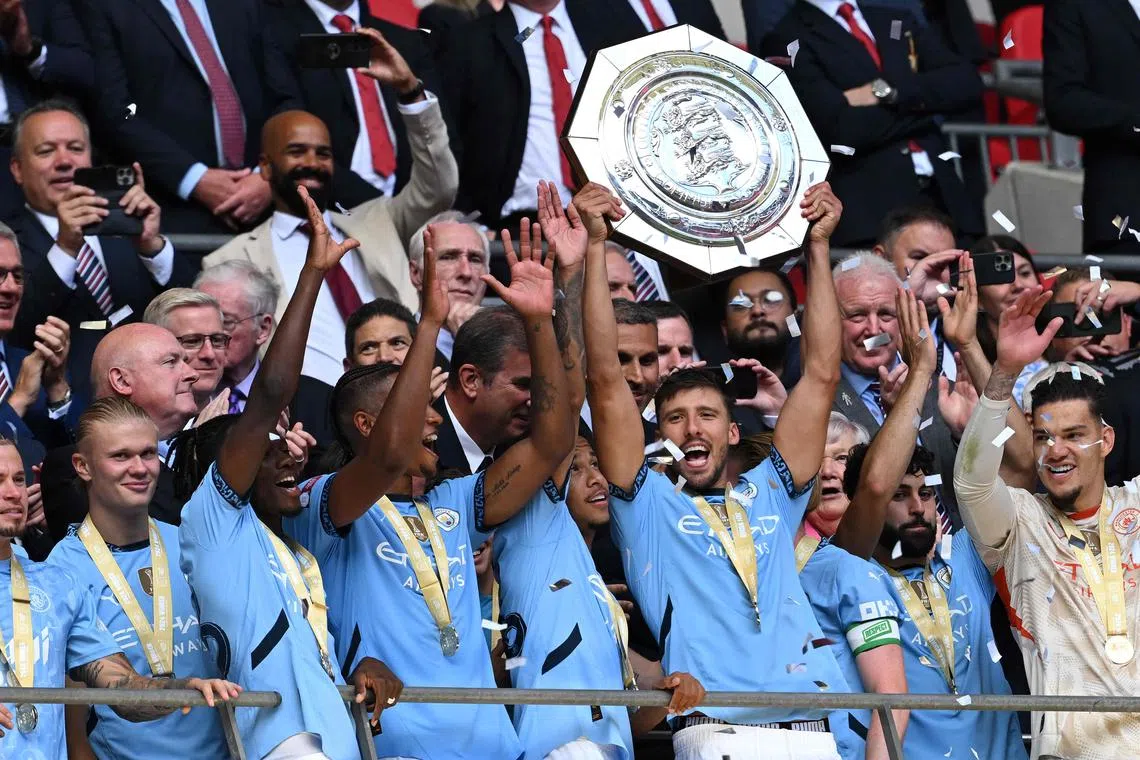 Manchester City's Portuguese defender #03 Ruben Dias holds aloft the trophy as the team pose after winning the English FA Community Shield football match between Manchester City and Manchester United at Wembley Stadium, in London on August 10, 2024. Manchester City  won after a 7-6 penalty shoot-out win, following the 1-1 draw in 90 minutes. (Photo by JUSTIN TALLIS / AFP) / NOT FOR MARKETING OR ADVERTISING USE / RESTRICTED TO EDITORIAL USE