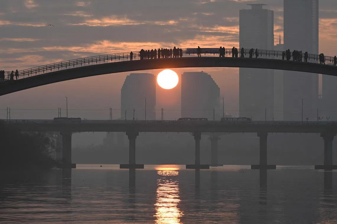 People watch the first sunrise of the new year from a footbridge overlooking the city skyline in Seoul on January 1, 2024. (Photo by Jung Yeon-je / AFP)