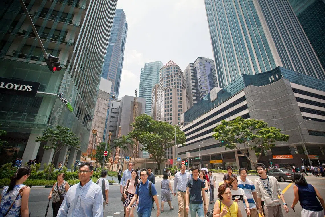 Pedestrians cross a road in the central business district of Singapore. 