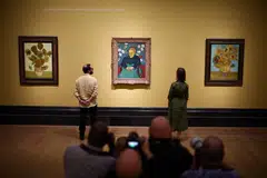 In a room with yellow walls, three paintings are notably exhibited: two “Sunflowers”, which surround  “The Lullaby”, a painting representing a woman, seated on an armchair.