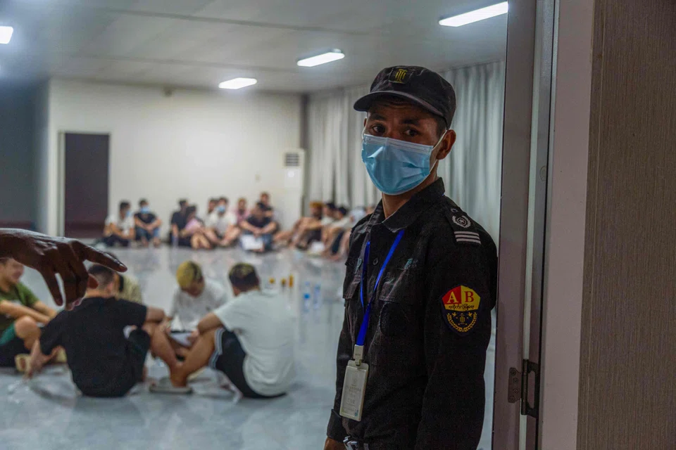 A security guard stands guard next to a room full of alleged scam centre workers and victims during a crackdown operation.
