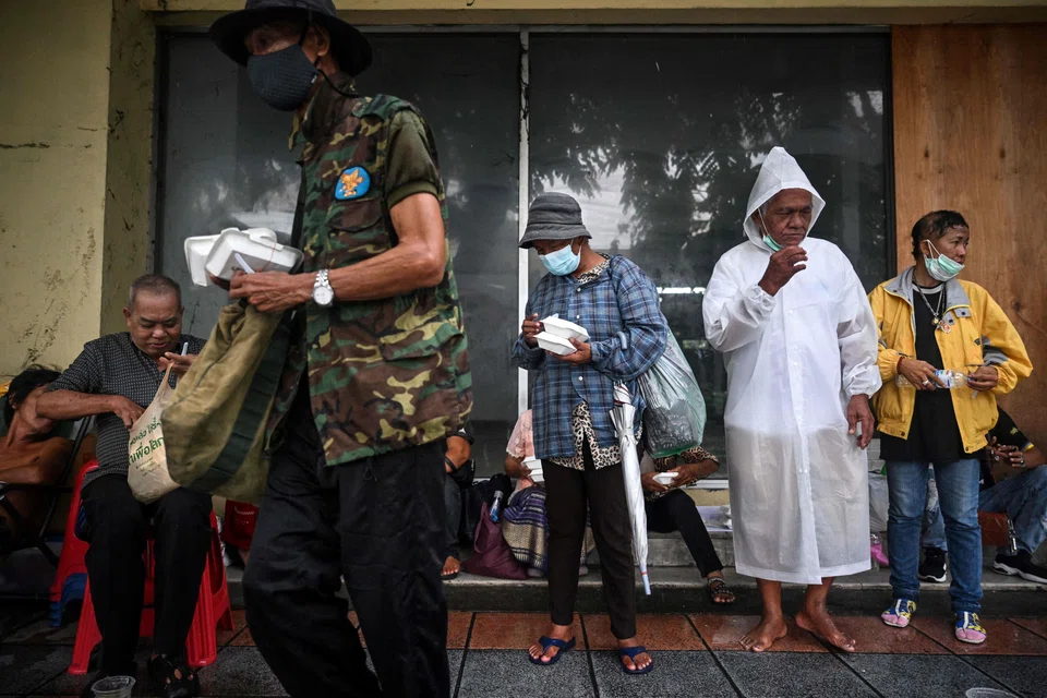 People sheltering from the rain after receiving meals from volunteers from Bangkok Community Help Foundation in Bangkok on Sep 13. Thailand is enduring a 14-year-high inflation which has caused soaring basic living costs.