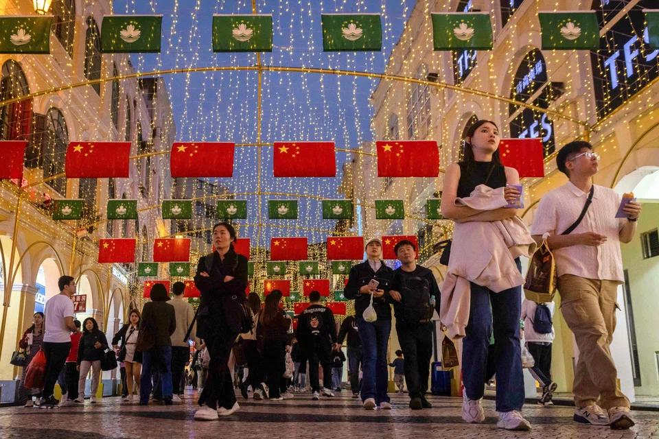 People walking underneath Macau and China flags at the Leal Senado Square in Macau, Dec 13, 2024.