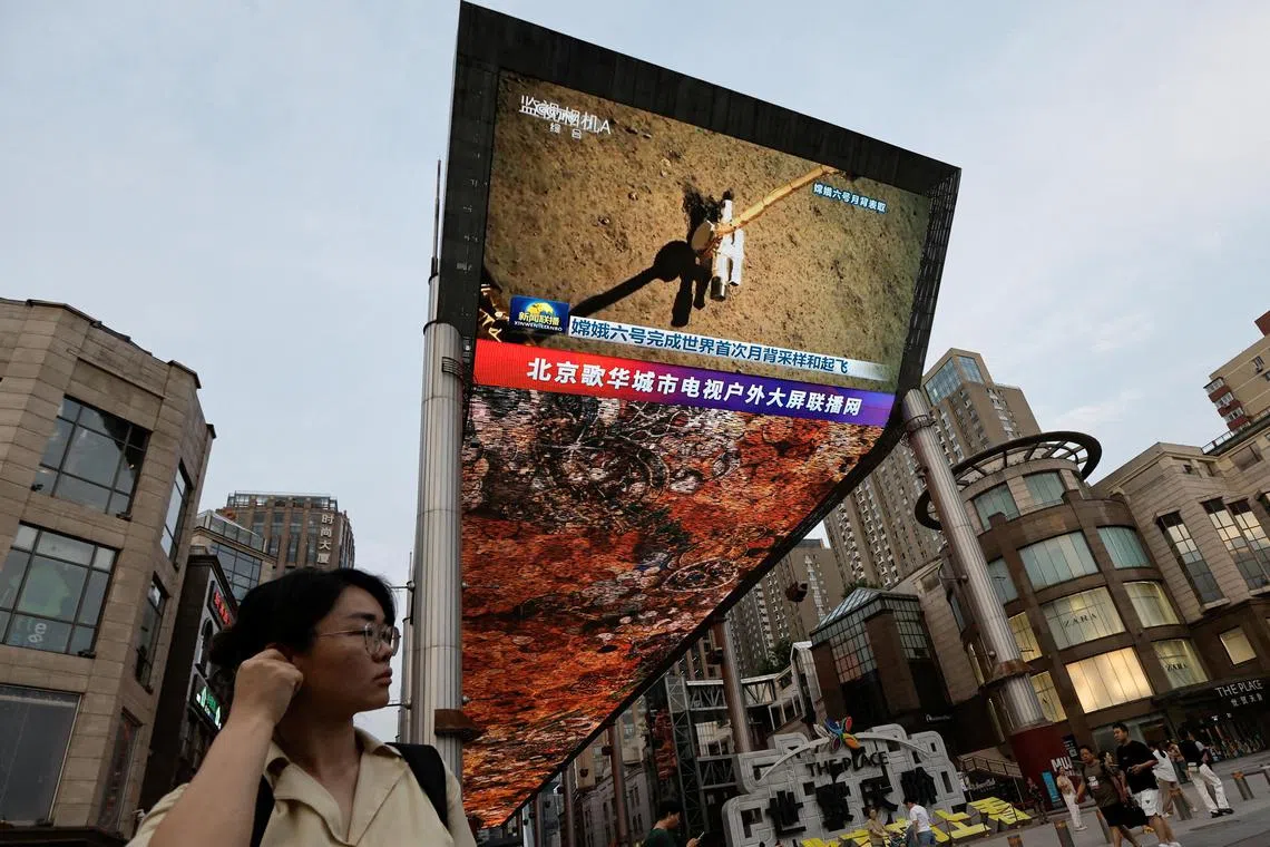 A large screen showing news footage of China's Chang'e-6 lunar probe on the far side of the moon. It drilled beneath the surface and sent back 2 kg of rock and dirt.