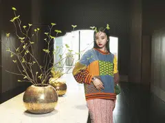Kōki, wears an oversized sweater, skirt by Kenzo, and a Serpenti Tubogas single spiral watch in stainless steel case and bracelet, with black opaline dial, by Bulgari.