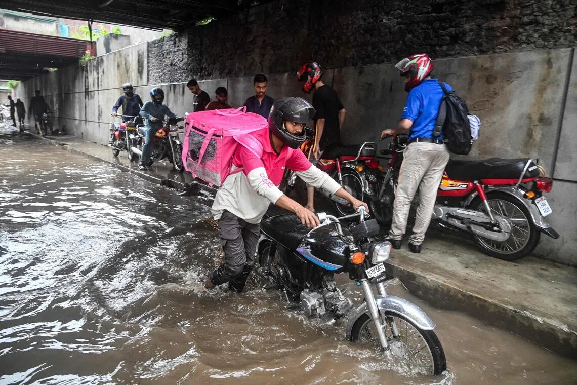 Foodpanda delivery rider Abdullah Abbas wades through a flooded street under a railway bridge after heavy rainfall in Lahore, Pakistan, Aug 30, 2025.