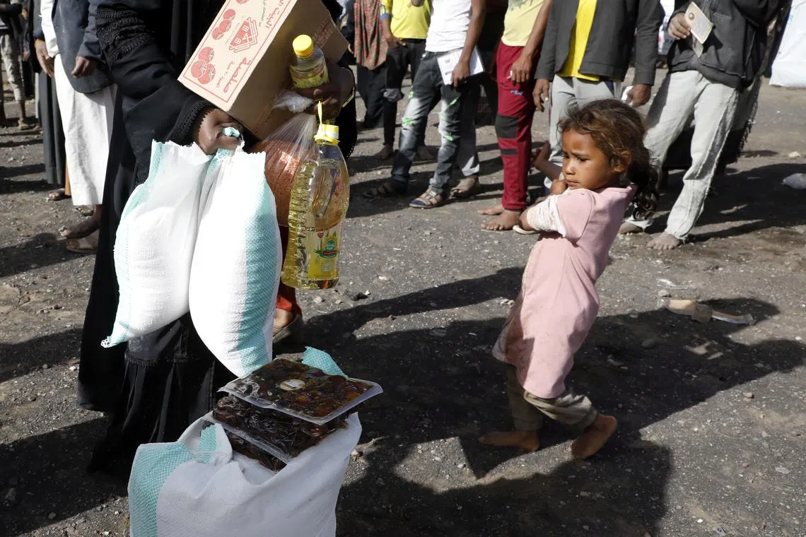 A Yemeni child waits for her mother receiving food aid, at a camp for Internally Displaced Persons (IDPs) on the outskirts of Sana'a, Yemen, April 2022. Years of civil war have resulted in severe food insecurity, and hence a crisis of hunger and malnourishment, for millions of Yemenis.