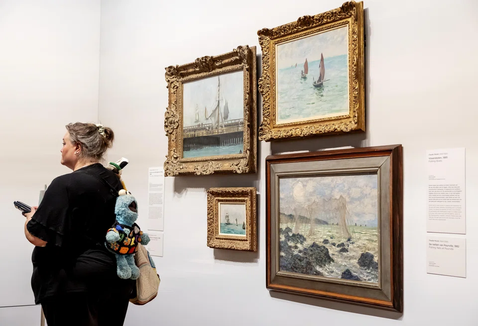 A woman looks at the works 'The Pier of Boulogne-sur-Mer' and 'Sailboats and Seagulls', by Edouard Manet, and 'Fishing Boats and The Nets of Pourville', by Claude Monet, from the new exhibition Vive l'impressionnisme! at the Van Gogh Museum in Amsterdam.