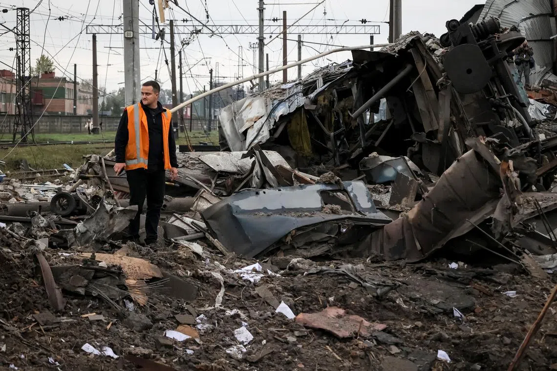 A worker stands near train cars at a freight railway station destroyed by Russian military strikes; Kharkiv, Ukraine, Sep 2022.  