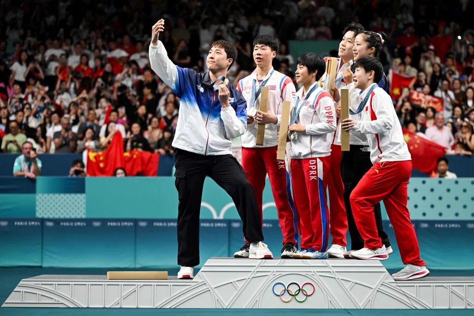 South Korea's Lim Jonghoon takes a selfie with his teammate and Chinese and North Korean mixed table tennis team medallists.