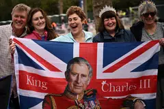Royal fans pose with a Union Jack flag depicting Britain's King Charles III  along the procession route, on The Mall, near to Buckingham Palace in central London.