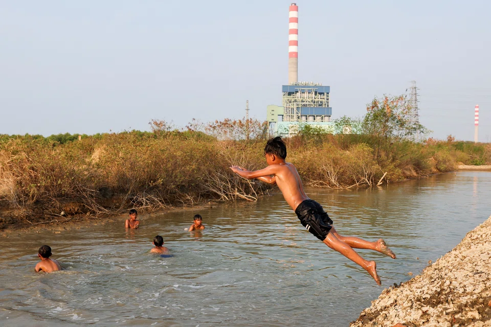 A boy jumps into the canal with one of Indonesia’s coal-fired power plants in the background, in West Java province. The world’s fifth-largest coal producer plans to retire some of such plants by 2030. 
