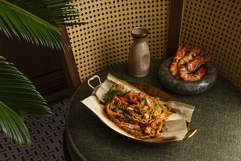 Grilled tiger prawns and flat noodles on opeh leaf.