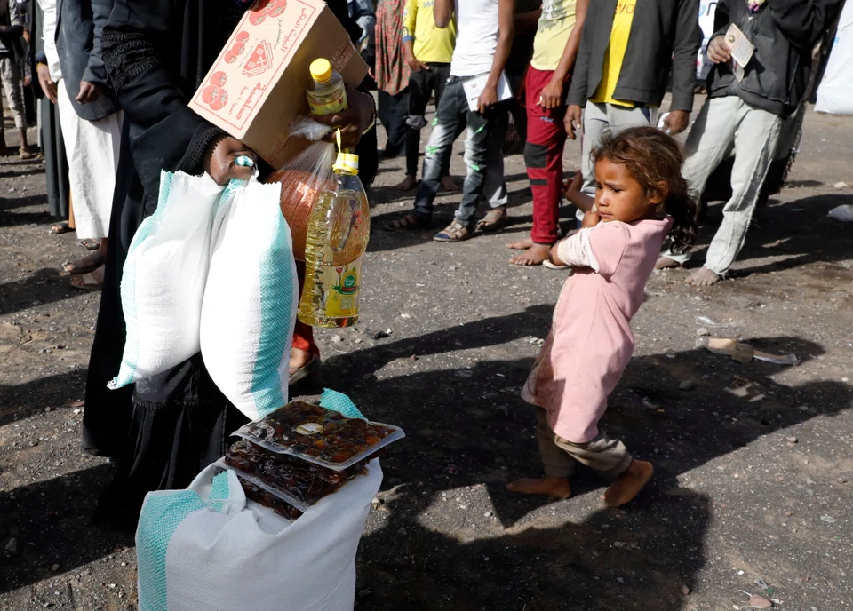 A Yemeni child waits for her mother receiving food aid, at a camp for Internally Displaced Persons (IDPs) on the outskirts of Sana'a, Yemen, April 2022. Years of civil war have resulted in severe food insecurity, and hence a crisis of hunger and malnourishment, for millions of Yemenis.