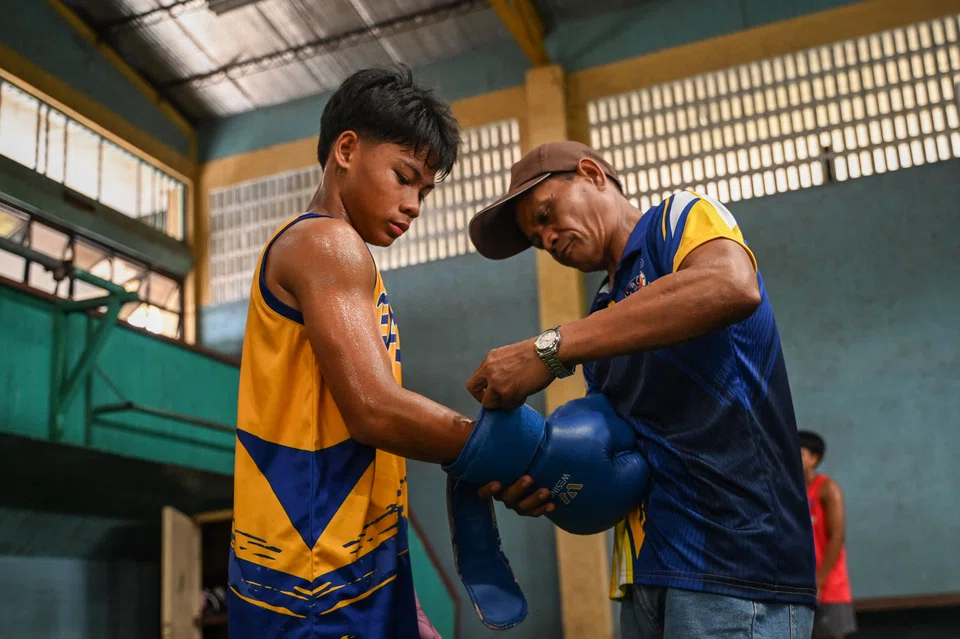 A youth receiving assistance with his gloves during training at a boxing gym in Bago City. Children from poor families get to work in pursuit of their Olympic boxing dream -- and a way out of poverty. 