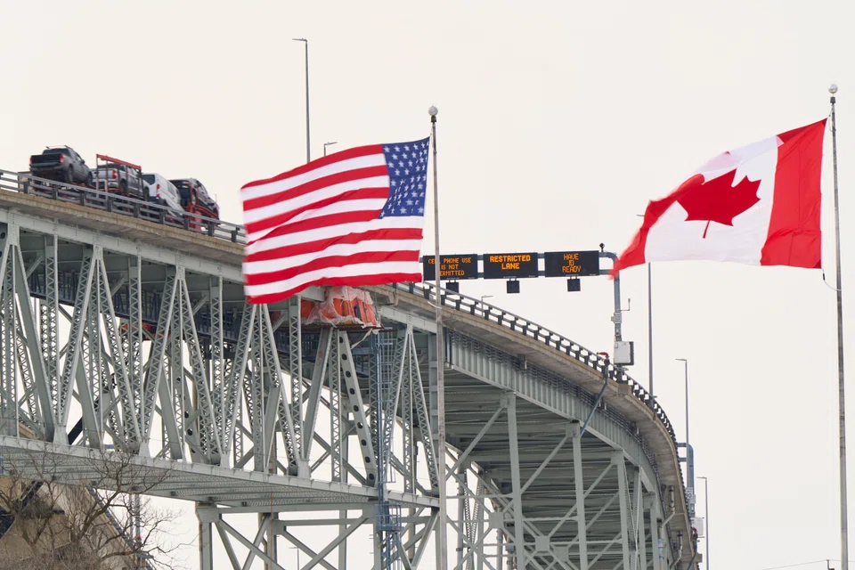 United States and Canadian flags fly on the US side of the St. Clair River near the Bluewater Bridge border crossing between Sarnia, Ontario and Port Huron, Michigan on Jan 29, 2025. US President Donald Trump's sweeping tariffs on Canada and Mexico are set to roil supply chains for products ranging from automobiles to avocados - with industries girding for cost increases.