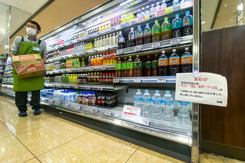 A staff member works as bottles of water with a sign written "bottled water is being rationed. 