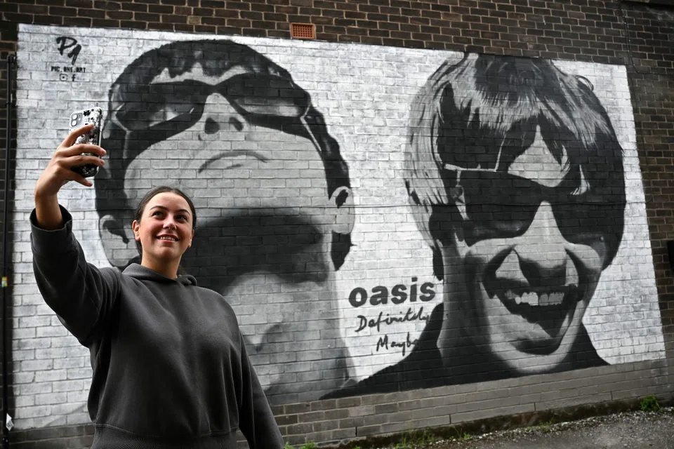 A fan takes a photograph with a mural depicting Oasis' Liam and Noel Gallagher on the side of Sifters Records in Manchester, Britain, Aug 27, 2024.