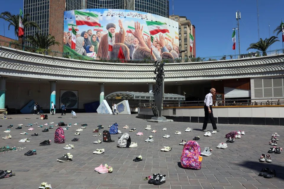 Symbolic belongings of Minab schoolgirls killed in a US airstrike were laid on the floor at Valiasr Square in Teheran on Apr 22, in front of a huge poster of the late Iranian supreme leader Ayatollah Ali Khamenei.