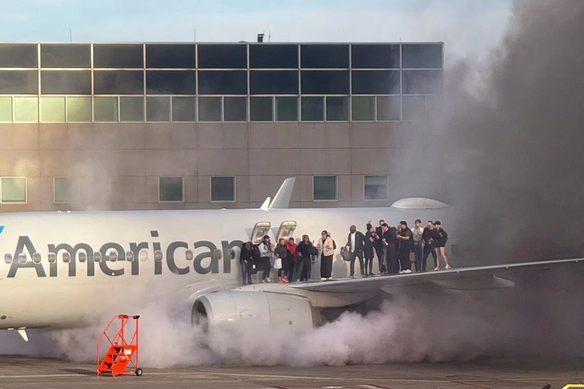Passengers standing on the wing of an American Airlines plane as they are evacuated after it caught fire while at a gate at Denver International Airport in Denver, Colorado, March 13, 2025. 