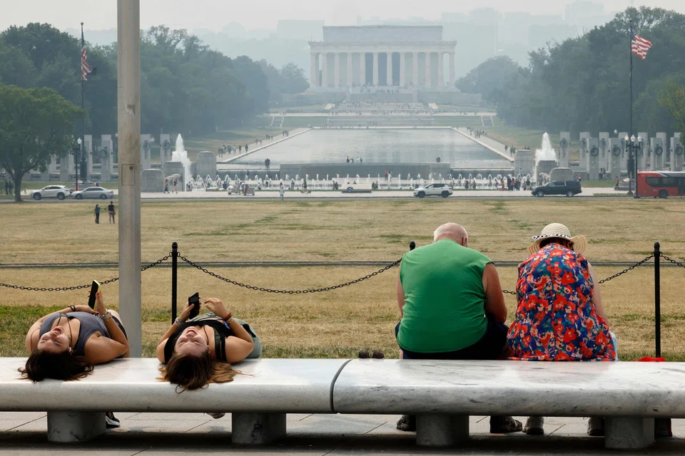 Tourists relax at the base of the Washington Monument as wildfire smoke leaves a veil of haze in front of the Lincoln Memorial along the National Mall on June 8, 2023 in Washington, DC. 
