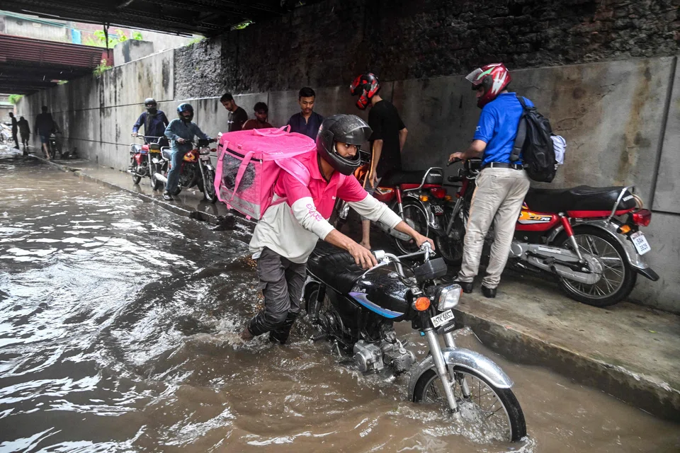 Foodpanda delivery rider Abdullah Abbas wades through a flooded street under a railway bridge after heavy rainfall in Lahore, Pakistan, Aug 30, 2025.