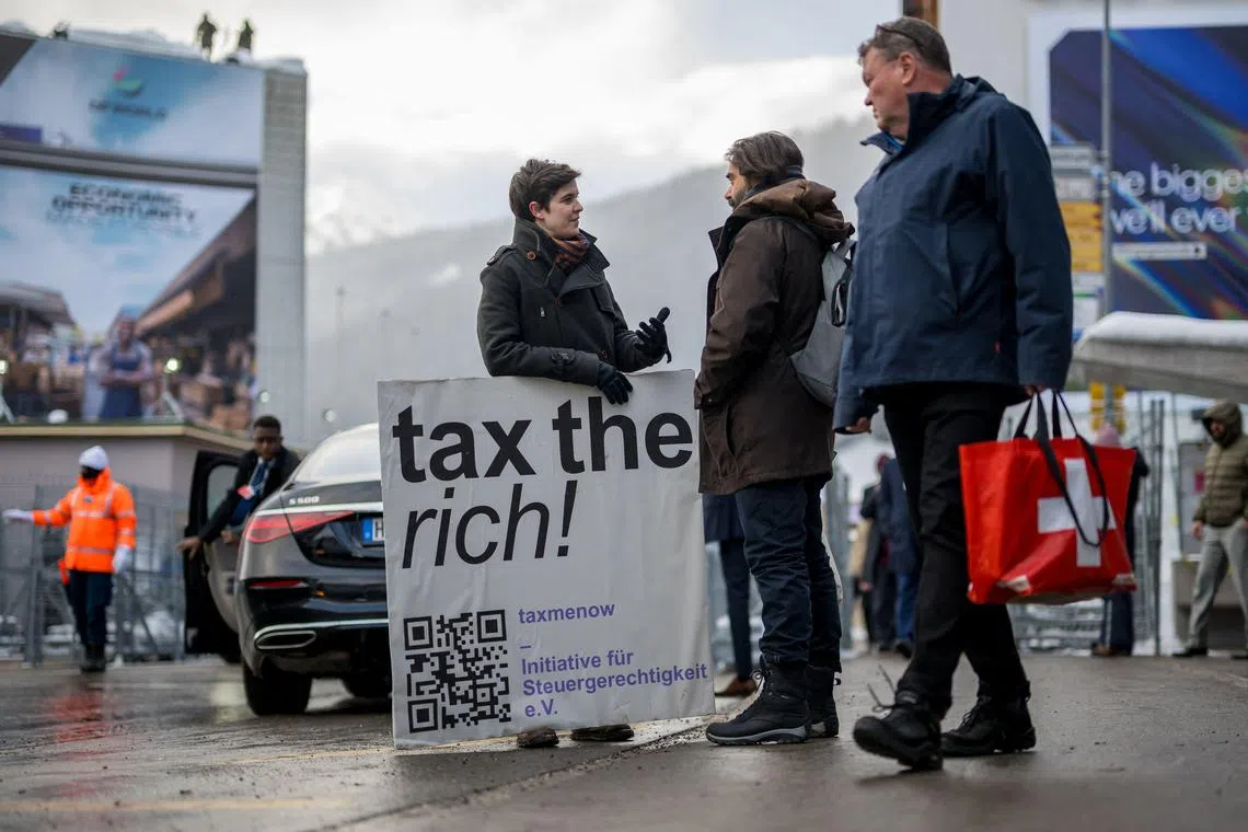 Austrian Marlene Engelhorn, from the family that owns Germany's chemical giant BASF, speaks as she holds a placard reading "Tax the rich!" at the entrance of the Congress Centre on the opening day of the WEF on Jan 15, 2024.