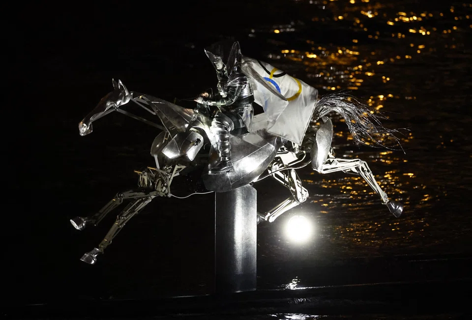 A woman on a robotic horse carrying a flag displaying the Olympic rings during the opening ceremony of the 2024 Paris Olympics, Paris, France, June 26, 2024.