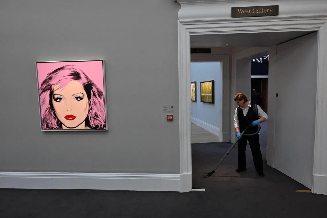 An employee works near Andy Warhol artworks at Sotheby's auction house in central London. Day jobs provide stability through the feast-or-famine cycles of gallery sales.