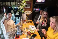 A tourist from the US (second left) sings karaoke as "mama-san" Kuri Awaji (left), who runs a snack bar, waves a glow stick at Kuriyakko in Tokyo, Japan, March 22, 2024. 