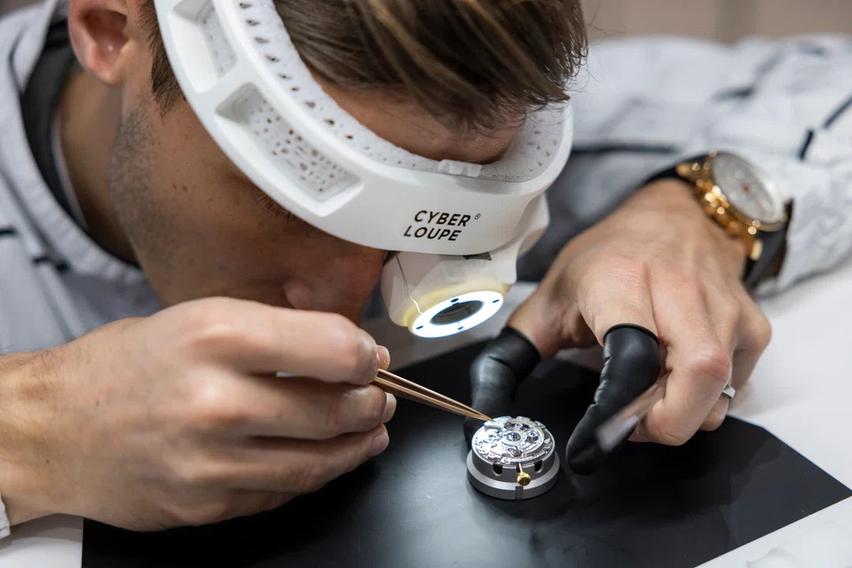 Caption: A watchmaker uses a futuristic cyber loupe to work on a movement at Watches and Wonders 2022 in Geneva