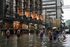 People walk along a flooded street in Manila amid heavy rains brought by Typhoon Gaemi, July 24, 2024.